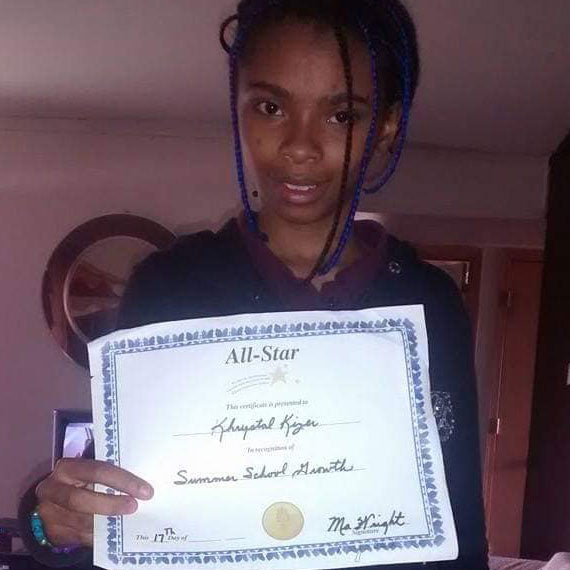 Image of Chrystul Kizer with braids in her hair holding up a certificate that reads 